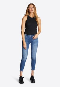Top senza maniche nero, jeans blu slim-fit e scarpe nere stringate. I jeans hanno un design sbiadito e una lunghezza cropped.