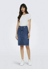 Dark blue denim skirt with a fitted design, knee-length, featuring a diagonal seam pattern and five-pocket styling. Paired with a white top and sneakers.