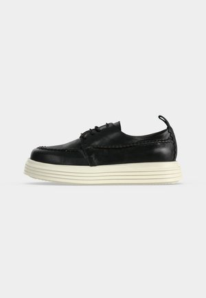 Black leather lace-up shoe with thick white ridged sole and pull tab on heel, shown from the side on a white background.