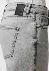 Sive traperice s visokim strukom, pet džepova i crnom kožnom oznakom na stražnjem dijelu struka s utisnutim natpisom "PIECES".