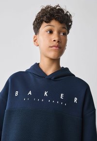 Námornícky modrá mikina s kapucňou s textúrovanou spodnou časťou, význačné biele logo "BAKER" a kapucňa so sťahovacou šnúrkou.