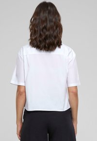 White short-sleeve top with a straight cut, featuring a back yoke, a slightly cropped hem, and smooth, lightweight fabric.