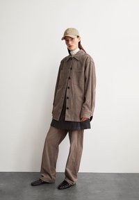 Braune Cordjacke mit großen Taschen, übereinander getragen über einem dunklen Hemd und einem hellen Rollkragenpullover. Kombiniert mit weitgeschnittenen braunen Hosen und mit Nieten besetzten Flats.