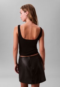 Μαύρο ριμπ τοπ με φαρδιές τιράντες συνδυασμένο με μαύρη δερμάτινη μίνι φούστα. Η φούστα έχει λεία υφή και διακριτικές ραφές.