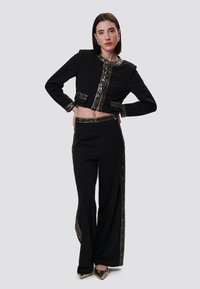 Zwarte cropped jas en flare broeken met gouden accenten en geometrische patronen. Glad stof met een gestructureerd ontwerp.