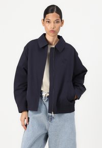 Sacou croppat bleu marin, cu guler chinezesc, fermoar frontal și buzunare laterale. Material moale cu detaliu brodat cu logo.