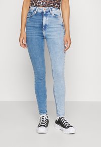 Höga smala jeans i ljusblå denim, med en blekt design och femficksstil, kombinerat med svartvita sneakers.