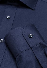 Navyblauwe shirt van een gestructureerde stof, met een klassieke kraag, knoopsluiting en een gedetailleerde manchette met een afgeronde rand en knoopaccent.