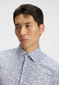 Witte shirt met een klein blauw bloemenpatroon, met een klassieke kraag en knoopsluiting. Soepele textuur en getailleerde pasvorm.