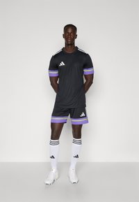 Zwarte sokkertrui en shorts met paarse en groene accenten, witte Adidas-strepen en bijpassende kniekousen met strepen en logo.