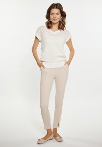 Lichtgewicht gebreide witte trui met ruitpatroon, gecombineerd met beige slim-fit broek met zijsplitten en lichte flats.