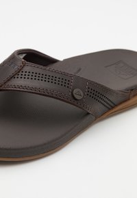 Bruine flip-flop sandaal met een gestructureerde band met perforaties, een gladde zool en een ronde logo-accent. Lichtgewicht ontwerp voor comfort.