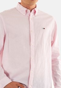 Camisa de botones de color rosa claro, hecha de lino, con un cuello clásico, mangas largas y un pequeño logo en el lado izquierdo del pecho.
