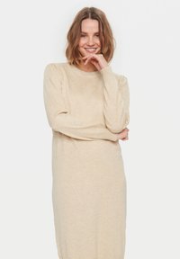 Beige stickad klänning med lång ärm, rund halsringning och mjuk textur. Har en lätt puff vid axlarna och en avslappnad passform.