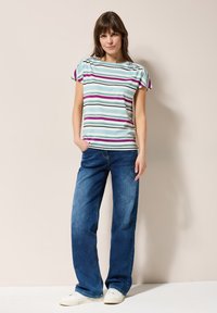 Stribet kortærmet top med vandrette lyseblå, lilla og grønne striber, parret med brede blå jeans og hvide sneakers.