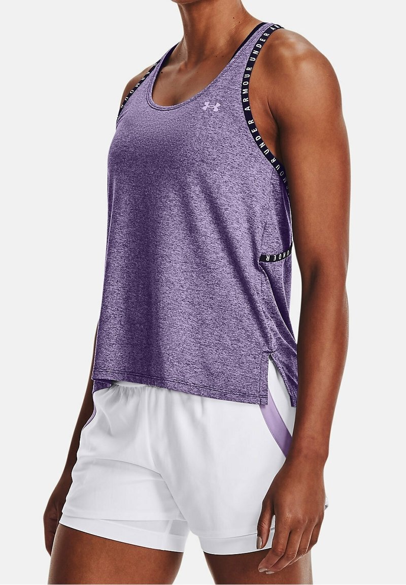 Lila atletisk linne med texturerad yta, med svarta band med "Under Armour"-logotyp, sidospjäll, kombinerat med vita shorts.