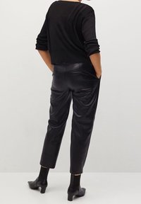 Pull court noir à texture côtelée avec trois coutures verticales au dos ; associé à un pantalon en cuir noir avec poches latérales.