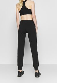 Schwarze sportliche Jogginghosen mit gerippten Bündchen, gefertigt aus einem glatten Stoff. Verfügt über ein konisch zulaufendes Bein und einen taillierten Bund.