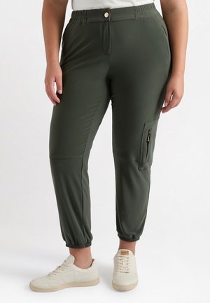 Joggers deportivos verdes de un material ligero, con una cintura elástica, bolsillo lateral con cremallera y puños ajustados, combinados con zapatillas blancas.