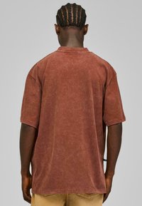 Rustfarget oversized t-skjorte laget av teksturert stoff, med korte ermer og rund hals. Bakvisningen fremhever et avslappet design.