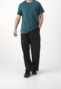 Teal bomullströja med svart Jordan-logga, kombinerad med vida svarta byxor och svarta skor. En enkel, avslappnad outfit.