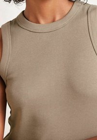 Débardeur côtelé de couleur fauve avec un col montant et un tissu texturé. Design simple sans éléments métalliques visibles ni motifs.