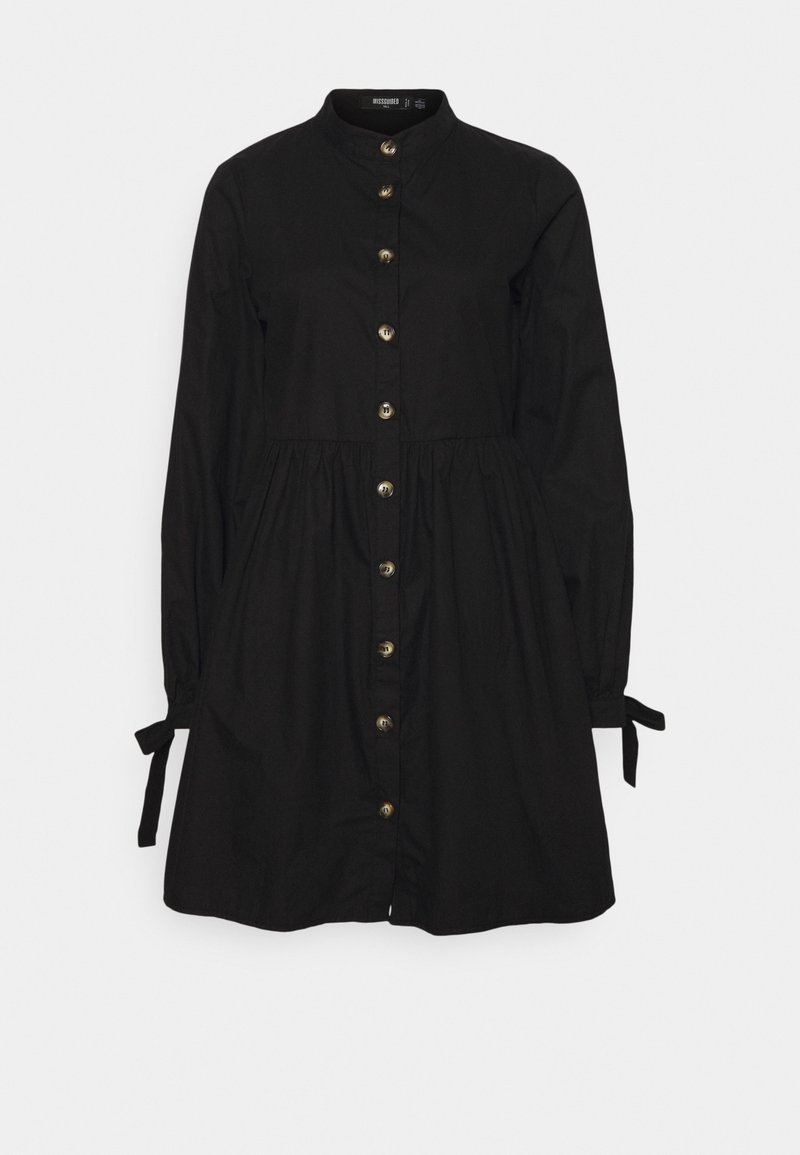 Černé košilové šaty s vysokým límcem, nařaseným pasem, dlouhými rukávy a vázáními na manžetách. Na přední straně jsou zlaté knoflíky.