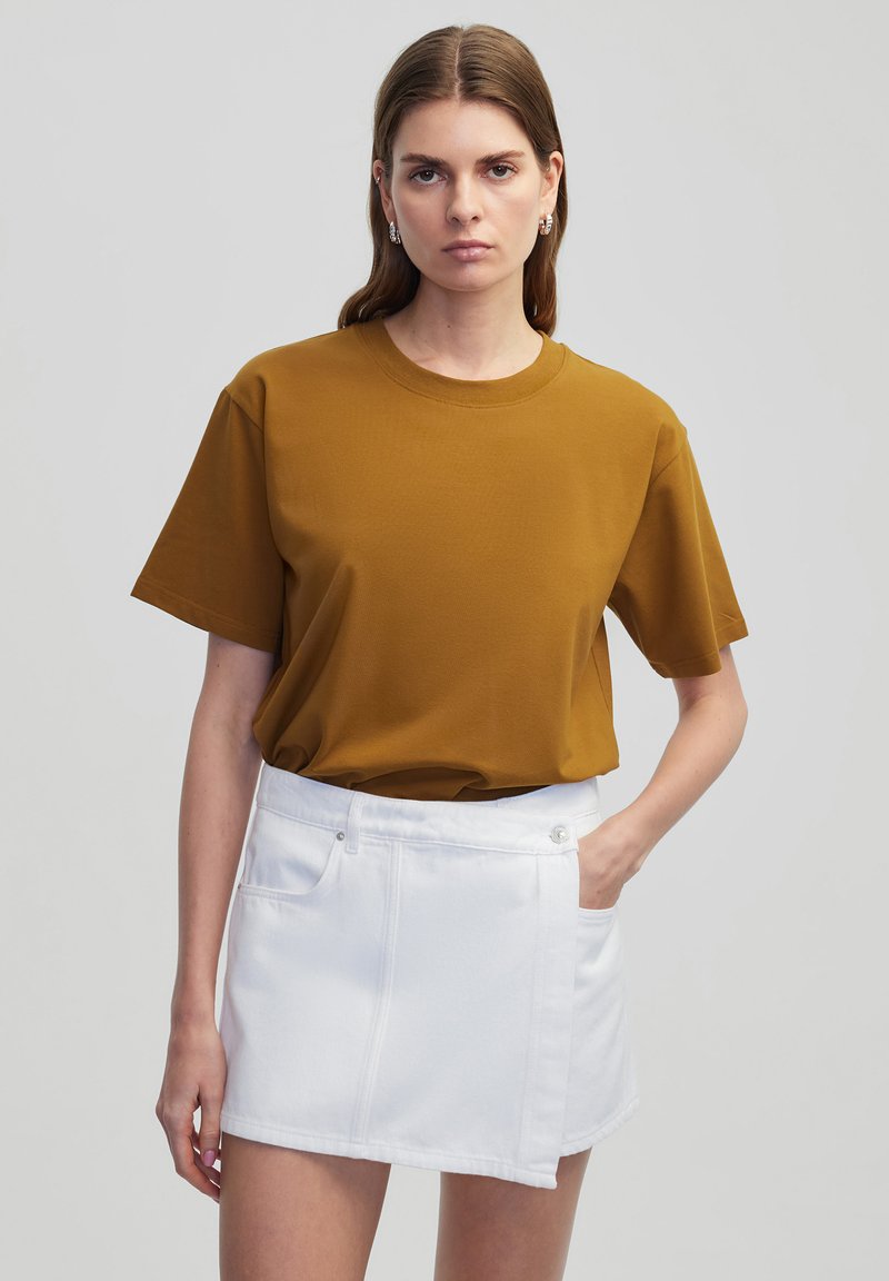 Mosterdgele katoenen t-shirt met korte mouwen en een ronde halslijn, gecombineerd met een witte denim minirok met een gestructureerd ontwerp en zijzakken.