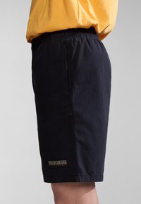Pantalones cortos azul marino hechos de una tela ligera, con una cintura elástica y un parche de logo en la pierna izquierda. Diseño simple, sin bolsillos visibles.