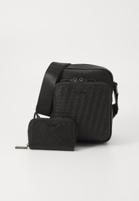 Černá crossbody taška vyrobená z texturovaného materiálu s vzorem herringbone, obsahující hlavní zipovou přihrádku a menší odpovídající peněženku.