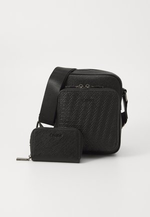 Sac crossbody noir en matériau texturé avec motif en chevrons, doté d'un compartiment principal zippé et d'un petit portefeuille assorti.