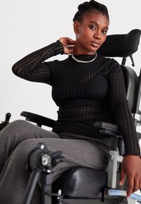 Top de manga longa preto canelado combinado com calças caneladas cinzas. A pessoa está sentada numa cadeira de rodas com um assento preto elegante e apoios de braços ajustáveis.