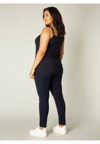 Marine casual tanktop en legging set. Zacht materiaal, slim fit ontwerp, met verstelbare bandjes en een soepele textuur. Gekleed met witte sneakers.