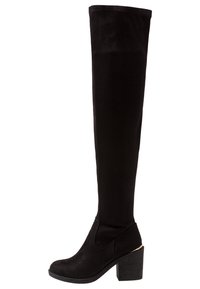 Botte montante noire en daim avec talon bloc et bout rond, présentant un subtil accent doré à la base du talon.