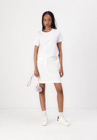 T-shirt en coton blanc associé à une jupe blanche, complété par un sac à main rose. Baskets blanches avec des accents noirs, chaussettes grises claires. Design simple.