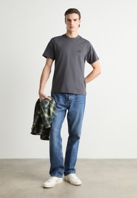 Grå bomulls T-skjorte med rund hals, kombinert med lyseblå jeans og holder en grønn rutete flanellskjorte. Hvite sneakers fullfører antrekket.