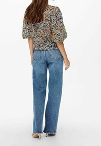 Blus med puffärmar i leopardmönster med beige, bruna och svarta nyanser; kombinerad med högmidjade blå denimjeans med rak ben.