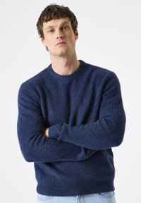 Marineblaues Strickpullover mit Rundhalsausschnitt, gerippten Bündchen und Saum. Weiche Textur mit einer leicht lockeren Passform. Trägt man mit hellblauen Jeans.