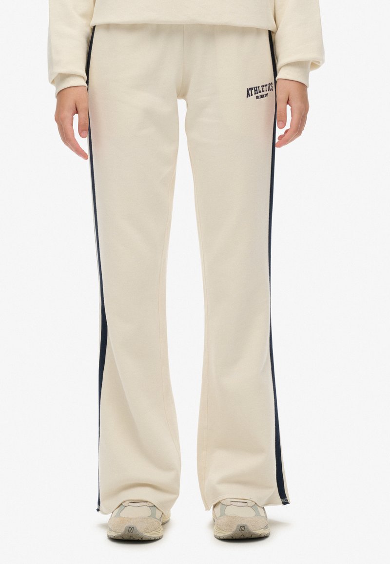 Creme-kleurige sportbroek met een recht model, voorzien van marineblauwe zijstrepen en een subtiele logo-opdruk aan de voorkant. Zachte materiaalsamenstelling.