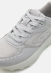 Light gray sneaker with mesh panels and leather accents. Features round laces, a padded collar, and subtle branding on tongue. Thick, textured sole.