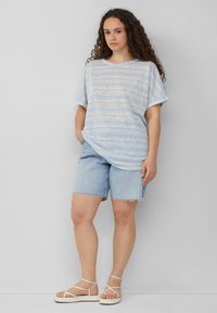 Lichtblauwe gestreepte T-shirt met een ontspannen pasvorm, gecombineerd met vervaagde denim shorts. Stevige witte sandalen maken de casual outfit compleet.