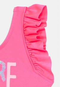 Haut de maillot de bain rose avec des bords froncés, texture lisse et accents irisés sur la lettre "F" dans une couleur contrastante.
