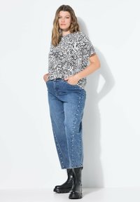 Černobílý vzorovaný krátký rukávový top spárovaný s modrými džíny s vysokým pasem a dekorativními cvočky, doplněný černými kotníkovými botami.