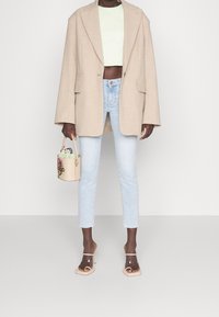 Beige Oversized-Blazer, hellgrünes, kurzes Rippoberteil, hellblaue gerade Jeans, transparente Riemchen-High Heels, kleine Handtasche mit floralem Muster.