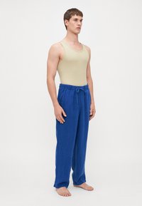 Tan tanktop laget av ribbet stoff, parret med løse, blå linbukser som har elastisk midje og snøring.