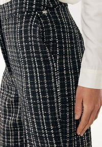 Svart och vit tweedbyxor med ett texturerat mönster, som har en figurnära design och en synlig varumärkesetikett på midjeresåren.