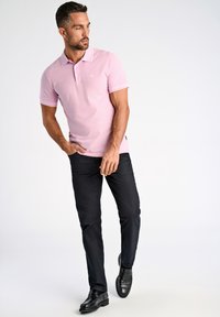 Camisa polo rosa con acentos blancos, combinada con pantalones negros y zapatos negros. La camisa presenta un pequeño logo de la marca en el pecho.