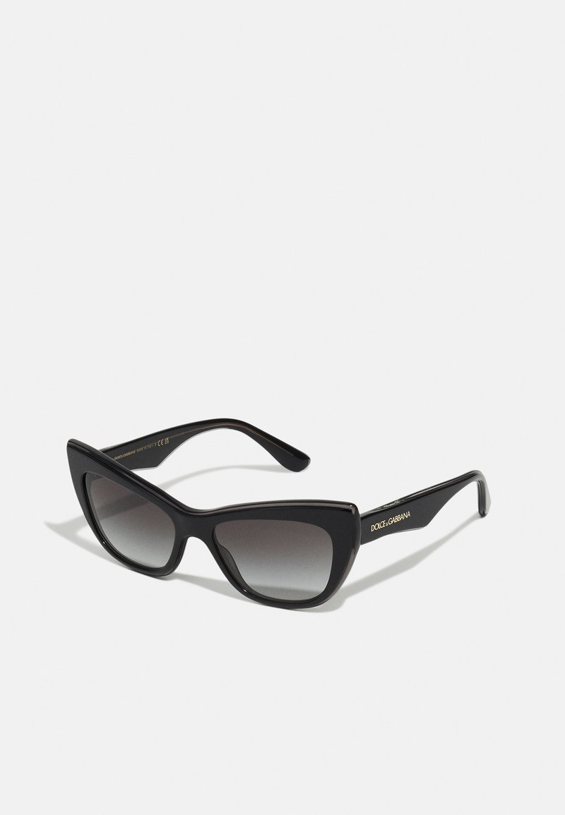 Black cat-eye sunglasses with gradient lenses, made of shiny plastic. Features a prominent angular design and gold logo accent on the arm.