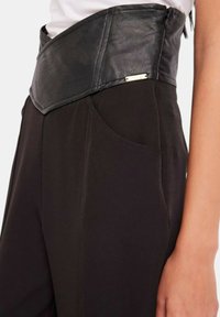 Pantaloni neri a vita alta con una cintura in pelle. Presentano una texture liscia, una tasca frontale e un dettaglio in hardware dorato.