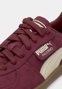 Gros plan d'une basket Puma Palermo bordeaux avec des lacets épais, un logo Puma blanc et une bande latérale beige sur une semelle marron.